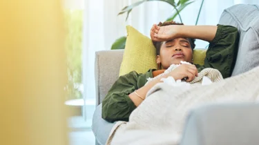 Kvinde ligger syg på sofaen.