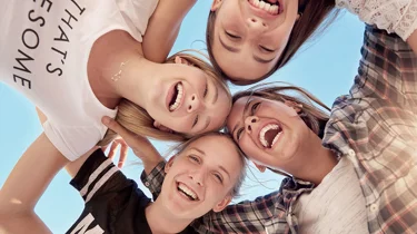 Et billede af gode veninder, der længer sig ind over kameraet og smiler og griner