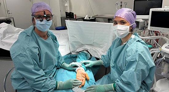 To kirurger med fuldt operationsudstyr kigger ind i kameraet.