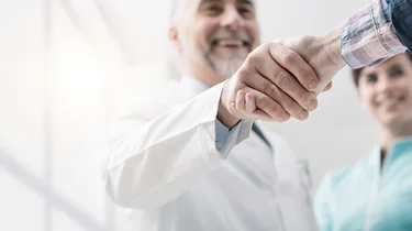 Læge giver smilende hånd til en patient.