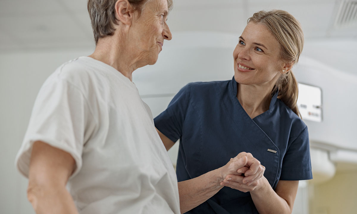 Sygeplejerske holder patient på skulder og smiler.