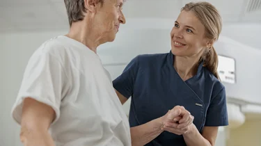 Sygeplejerske holder patient på skulder og smiler.