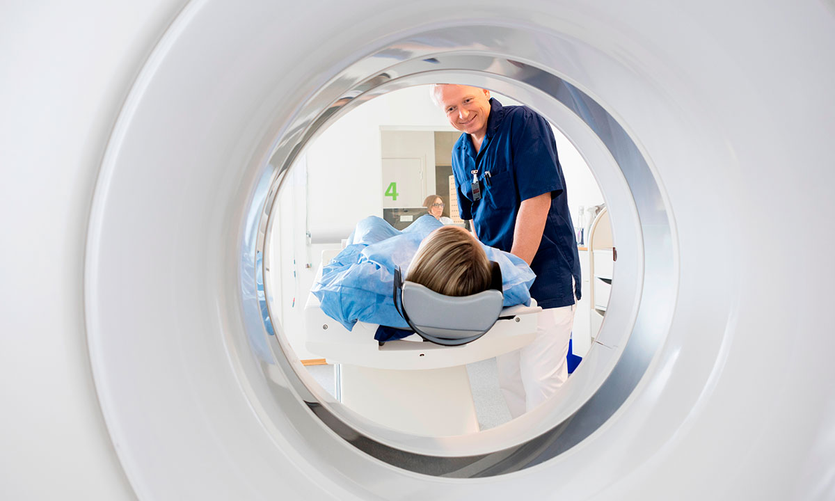 Patient ligger i en CT-scanner, mens radiograf hjælper på plads.