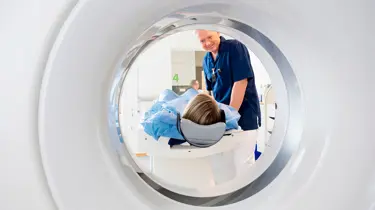 Patient ligger i en CT-scanner, mens radiograf hjælper på plads.