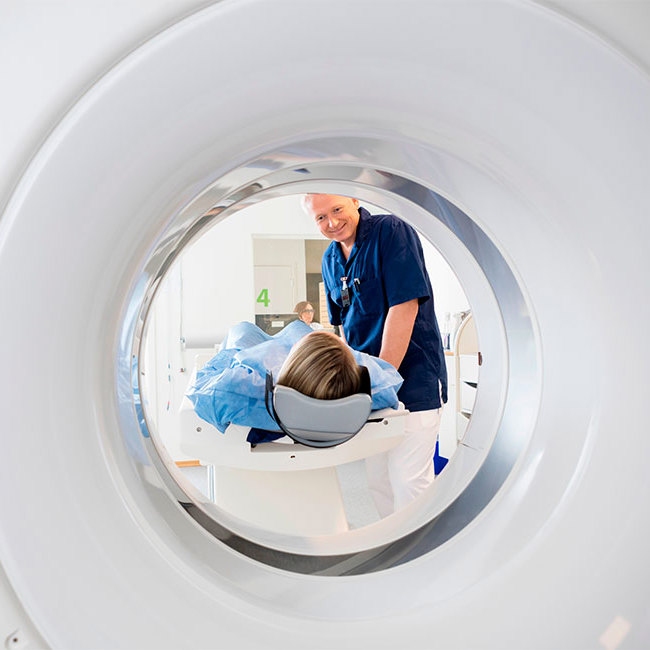 Patient ligger i en CT-scanner, mens radiograf hjælper på plads.