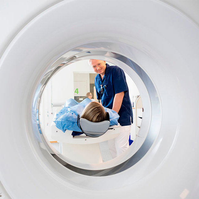 Patient ligger i en CT-scanner, mens radiograf hjælper på plads.