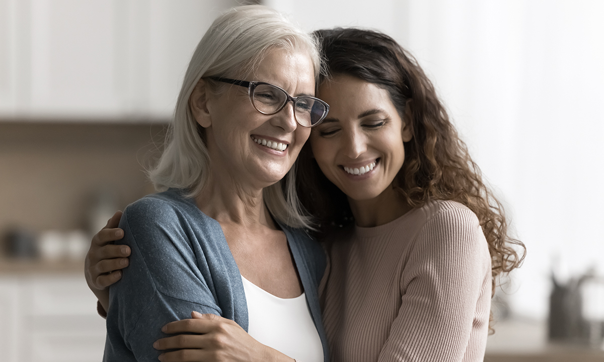 En mor og datter sidder i en sofa og holder om hinanden.