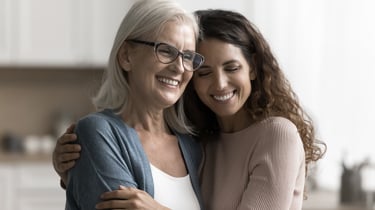 En mor og datter sidder i en sofa og holder om hinanden.