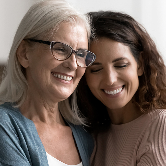 En mor og datter sidder i en sofa og holder om hinanden.