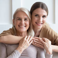 Et portræt af en mor og voksen datter, som holder om hinanden og smiler til kameraet