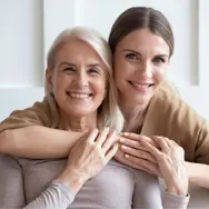 Et portræt af en mor og voksen datter, som holder om hinanden og smiler til kameraet