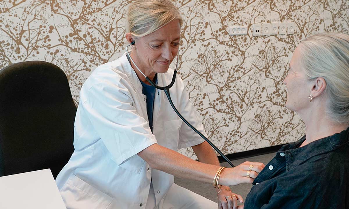 Helbredslæge lytter til hjertet på en patient.