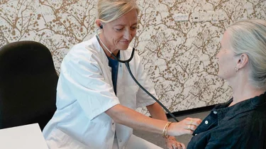 Helbredslæge lytter til hjertet på en patient.