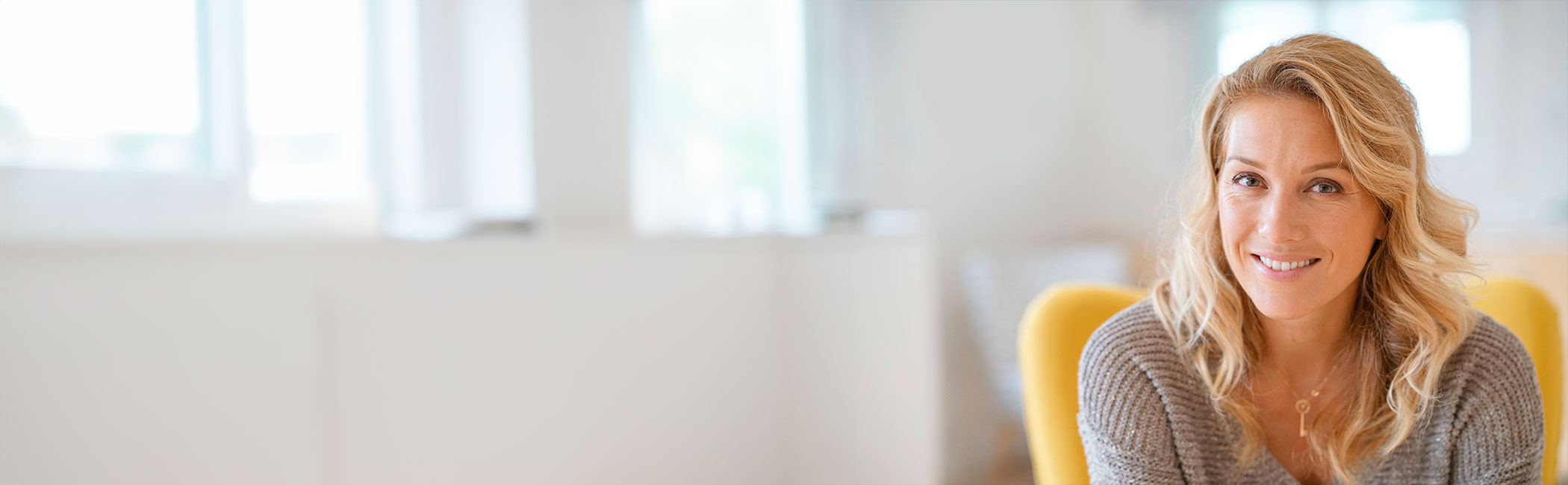 Kvinde 40+ sidder i en gul stol og smiler in i kameraet.