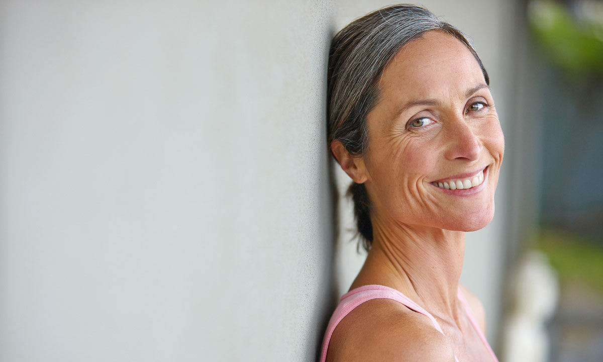 Midaldrende kvinde læner sig op ad en væg og smiler ind i kameraet.