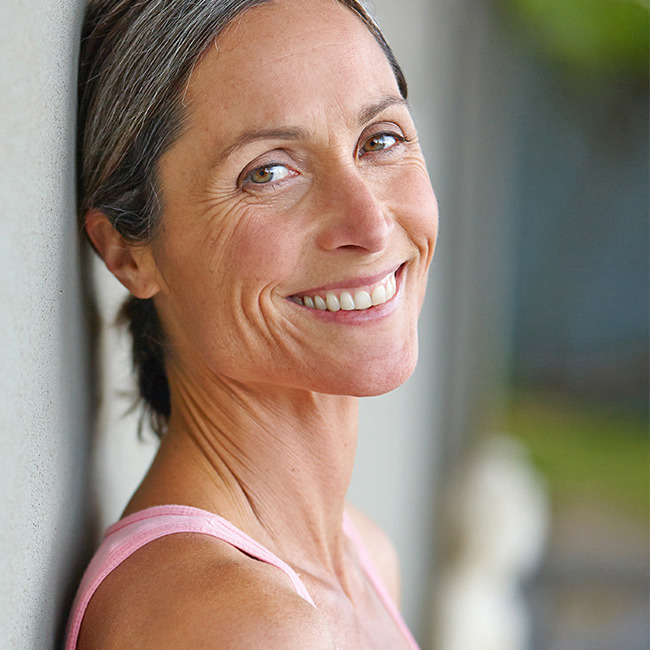 Midaldrende kvinde læner sig op ad en væg og smiler ind i kameraet.