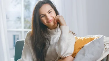 Glad kvinde sidder i sofa og smiler.