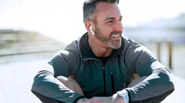 Glad mand sidder i naturen og lytter til musik.