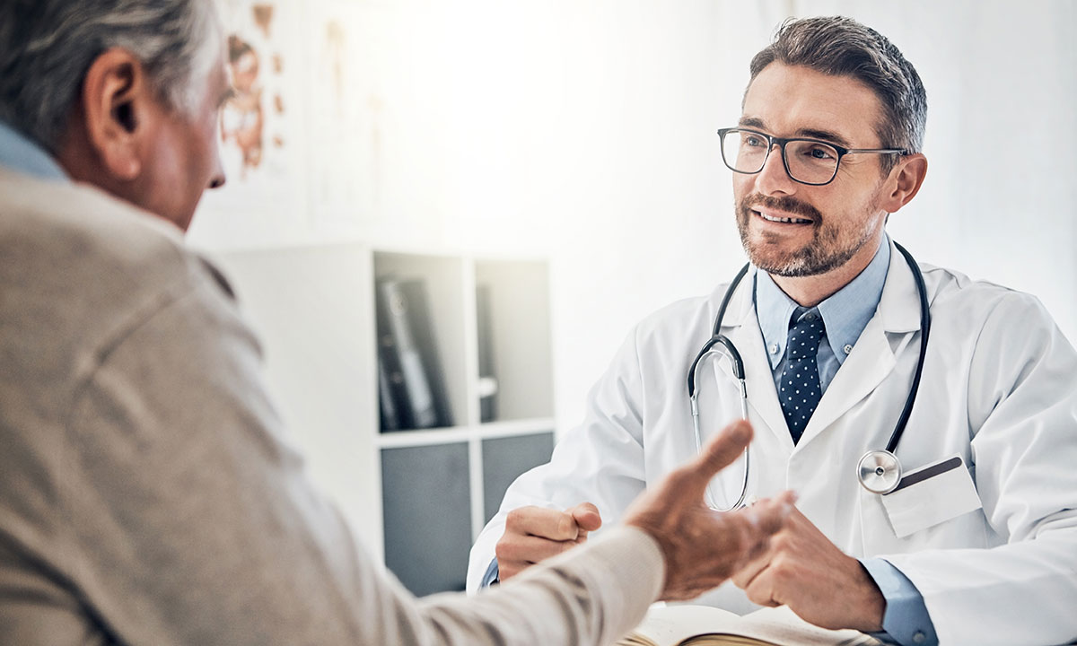 Mand sidder hos lægen og får forklaret mulige helbredsundersøgelser hos Aleris.