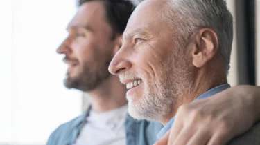 Portræt af en far og en voksen søn med armen om hinanden, som skuer ud i horisonten.