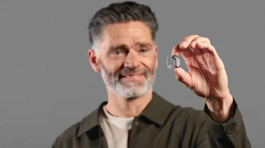 Mand holder lille Oticon RITE høreapparat mellem fingrene