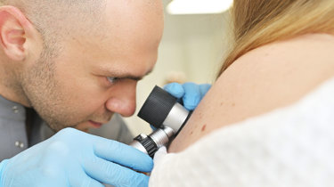 Hudlæge undersøger patients hud med dermatoskop.
