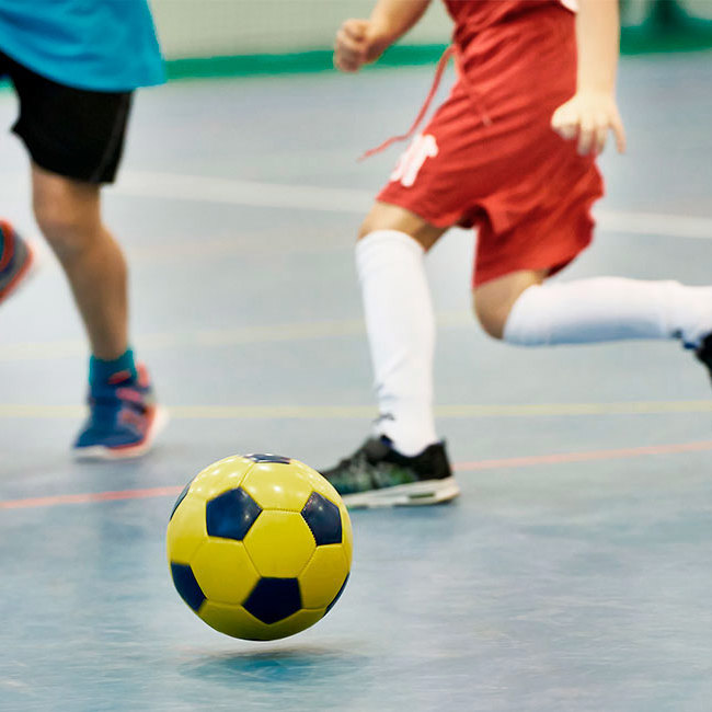To børn spiller fodbold i en hal.