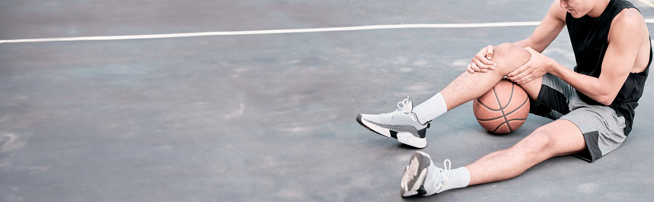 Basketballspiller sidder på jorden og holder på sit knæ.