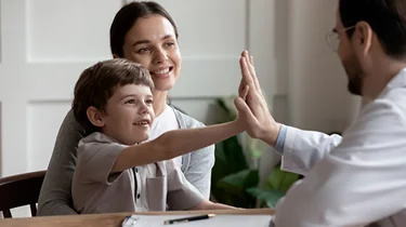Mor og barn sidder smilende ved en børneortopædkirurg.