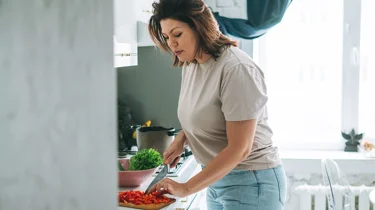 Kvinde står og forbereder mad i køkken efter råd fra en diætist.