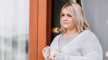 Overvægtig kvinde står i havedør og kigger ud.