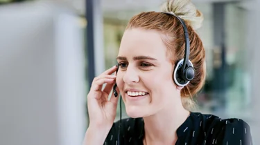 En medarbejder i Aleris kundeservice sidder og taler med en patient i telefon med headset på.