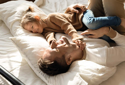 Far og datter ligger i sengen og griner.