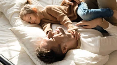 Far og datter ligger i sengen og griner.