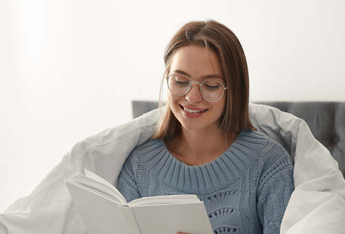 Glad ung kvinde sidder i en seng med dynen om sig. Hun kigger ned på noget.