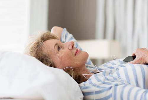 Glad kvinde ligger på ryggen i sengen med høretelefoner på.