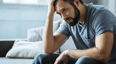 Mand sidder i sofa og ser trist ud.
