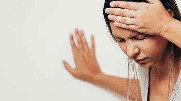 En svimmel kvinde tager sig til hovedet og støtter sig til væggen.