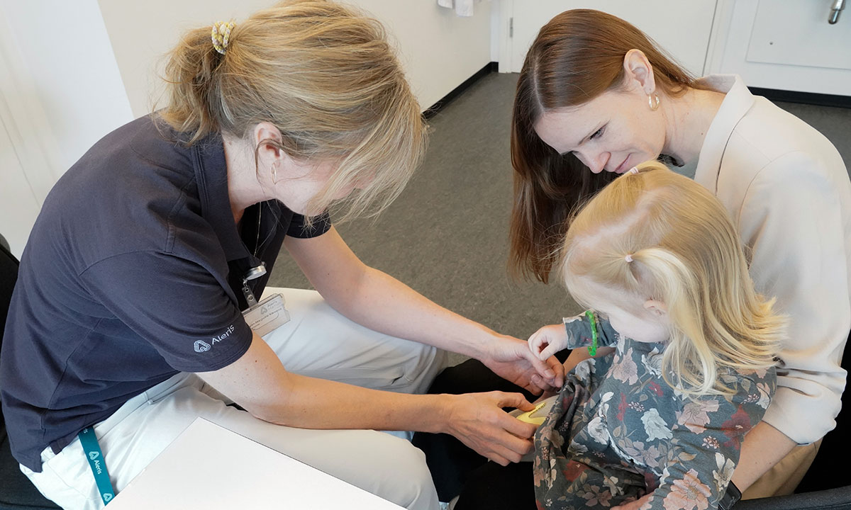 Sygeplejerske vaccinerer et barn, som sidder i sin mors favn.